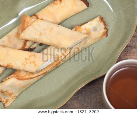 Delicious cheese blintz on green plate and cup of tea on wooden vintage tray