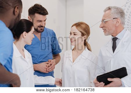 Meeting new young colleague. Kind friendly positive doctors enjoying working hours in the clinic and working in one team while expressing positivity and getting acquainted with new staff member