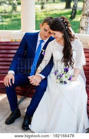 Beautiful young bride and groom sitting on a bench and holding hands.Wedding couple in love at wedding day