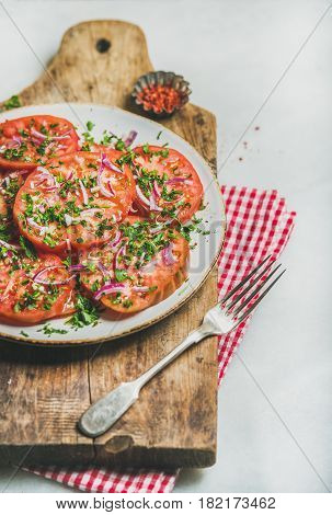Fresh heirloom tomato, parsley and onion salad in white plate on serving wooden board over light grey marble background, selective focus. Clean eating, vegan, vegetarian, healthy, dieting food concept