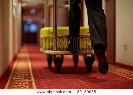 Porter moving luggage in cart down aisle covered by red carpet