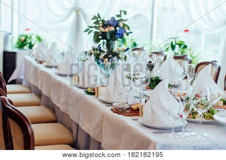 Table setting. Table served for wedding banquet close up view. White napkin on a white empty plate on a dining table
