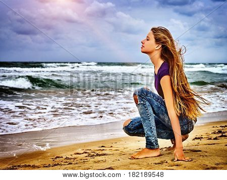 Girl on in sand beach looks thoughtfully into distance to last ray of sunset, falling on hectic sea. Art photography was taken in spring or summer. Woman in love .