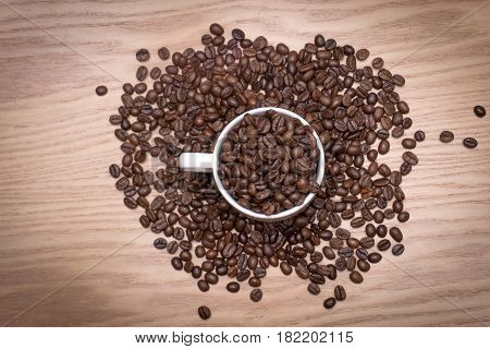TOP VIEW: Coffee beans in a white cup and on wooden table.
