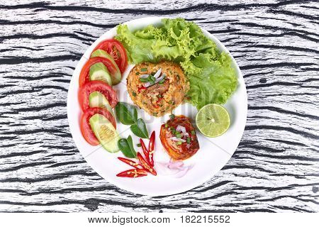 Thai food Fried jasmine rice with canned fishmackerel in tomato sauce topped halve green lemonsliced tomatocucumberred chilired onionlettuce and kaffir lime leaves.