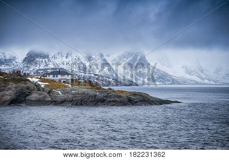 Travel and Tourism Concepts. One Separate House on Seashore Coastline in Norway Against Mountains Covered With Snow.Horizontal Image Composition