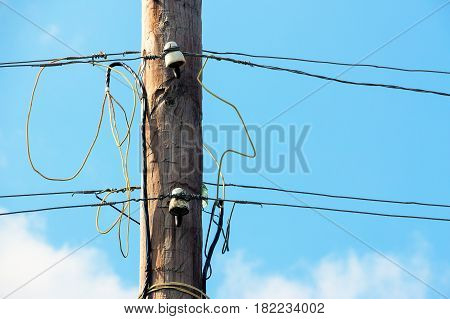 Old wooden pillar with power line against the blue sky. A botched electrical connections