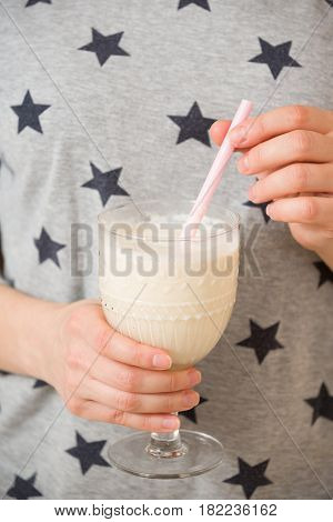 Young woman with a big glass of healthy smoothie served with a straw and oats. Hands holding milkshake. Stars background. Dairy snack or breakfast.