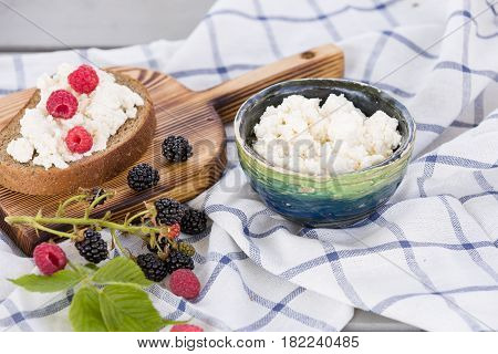 Organic Farming Cottage cheese in a green bowl slice of whole wheat bread with Homemade Ricotta cheese served with raspberries and blackberries on wooden board on linen fabric