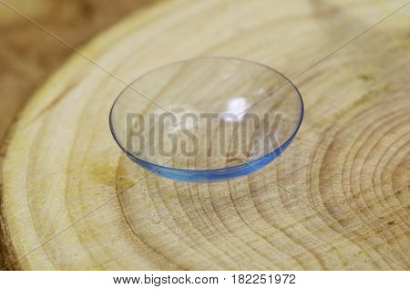 A soft contact lens lies on a wooden surface