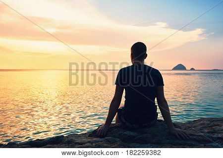 Contemplation at the beautiful sunset. Silhouette of the young man on the beach.