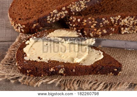 slice of black bread with sesame seeds and butter on an old wooden background.