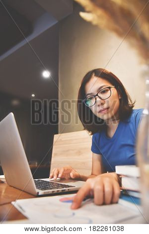 Asian eyeglasses Woman using laptop with graph financial diagram documents on wooden table.