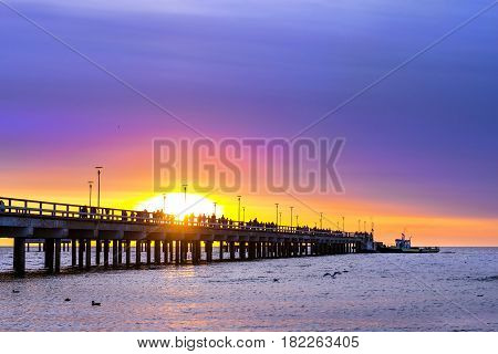 Ferroconcrete pillars of pedestrian seaside pier set in water on coast of Baltic sea. Passenger barge moored to bridge at sunset in resort Palanga Lithuania. Industrial & civil architectural design
