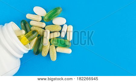 Vitamin complex omega 3 glucosamine capsules multivitamin supplements and white container on blue background top view.