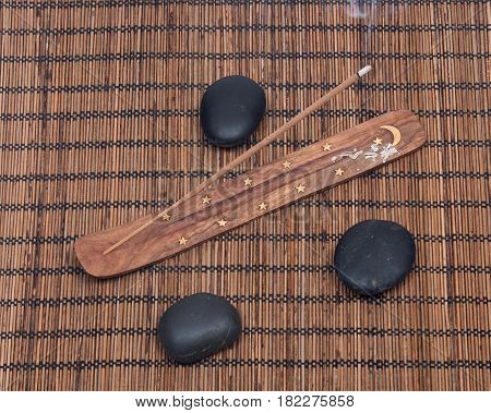 Hand carved burner, holder with sandalwood incense and polished black river pebbles on bamboo placemat