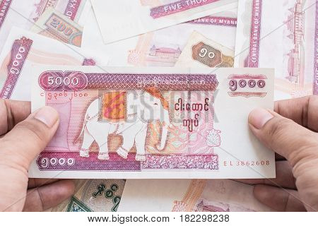 5,000 of Myanmar kyat banknote on hand with currency background.