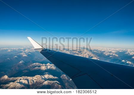 Looking through the window aircraft during flight a snow covered Italian and Osterreich Alps with blue sky without clouds.