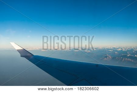 Looking through the window aircraft during flight a snow covered Italian and Osterreich Alps with blue sky without clouds.