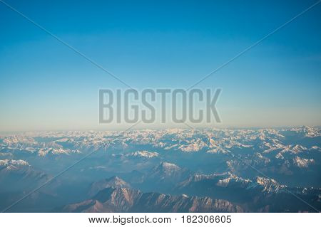 Looking through the window aircraft during flight a snow covered Italian and Osterreich Alps with blue sky without clouds.