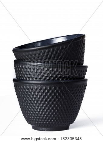 Stacked black traditional tea cups of cast iron isolated on white background.