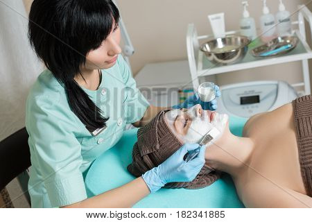 beautician applies face mask on the beautiful young woman in Spa salon. cosmetic procedure skin care. Microdermabrasion