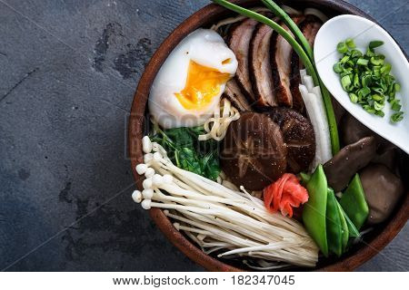 Ramen noodles bowl with egg, enoki, shiitake mushrooms, duck and onion, dark background, close view