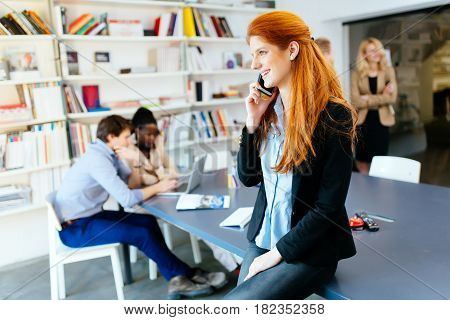 Beautiful businesswoman using phone in office while colleagues work in background