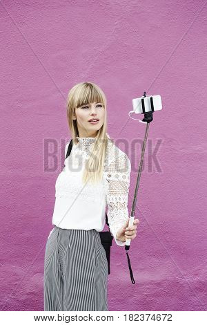 Blond and beautiful woman posing for selfie against pink