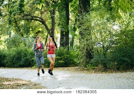 Energetic young women running outdoors in park to keep their bodies in shape