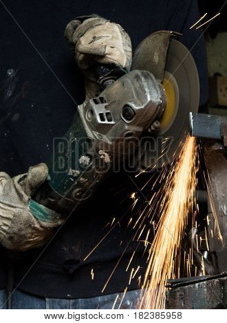 Craftsman uses angle grinder to cut piece of wrought iron metal with sparks flying and protective industrial gloves