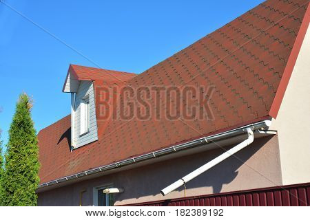 Old Roof Asphalt Shingles with Moss. Rain Gutter Pipeline with Downspout Pipe and Attic Mansard Window. Roofing Construction Roofing Repair.