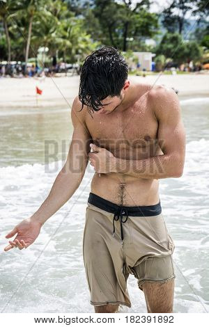 Young shirtless male standing in water of ocean and checking arm stung by jellyfish.