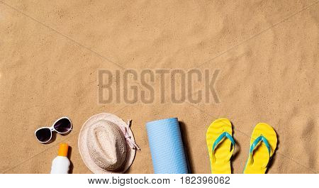 Summer vacation composition with pair of yellow flip flop sandals, hat, sunglasses, sun cream and other stuff on a beach. Sand background, studio shot, flat lay. Copy space.