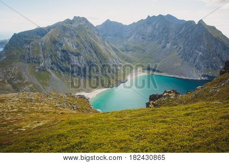 Beautiful Vibrant Norwegian Mountain Landscape from Ryten peak - famous mountain in Lofoten Islands, Moskenes municipality, Nordland with a view of Kvalvika beach, with hiking tourists and blue sky
