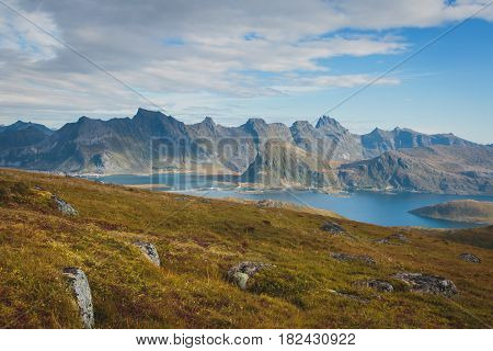 Beautiful Vibrant Norwegian Mountain Landscape from Ryten peak - famous mountain in Lofoten Islands, Moskenes municipality, Nordland with a view of Kvalvika beach, with hiking tourists and blue sky
