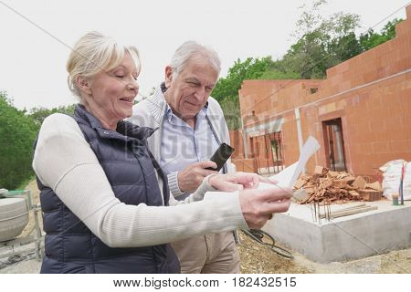 Senior couple in building site checking plans of their future house