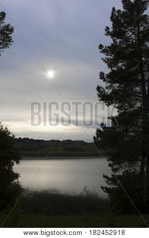 Full moon in cloudy dusk sky with lake reflection