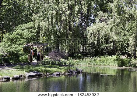 Laval, Quebec - June 14, 2015 - Landscape of a woman standing in a small wooden rest stop beside a man made lake in the Nature Park, Laval, Quebec on a sunny day in June.