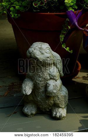 Concrete bunny in morning light with colorful plants in terra cotta planter in background