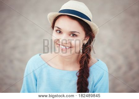 Closeup portrait of beautiful smiling white Caucasian brunette girl with brown eyes and plait in blue dress and straw hat looking in camera rustic retro vintage style concept