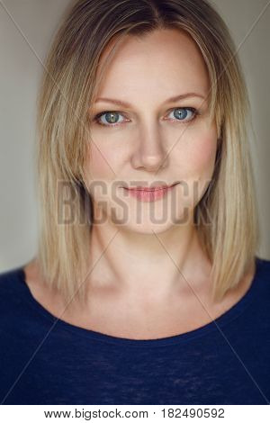 Closeup portrait of beautiful young middle age Caucasian woman in blue shirt looking in camera with long blonde hair bob and blue eyes flirty look