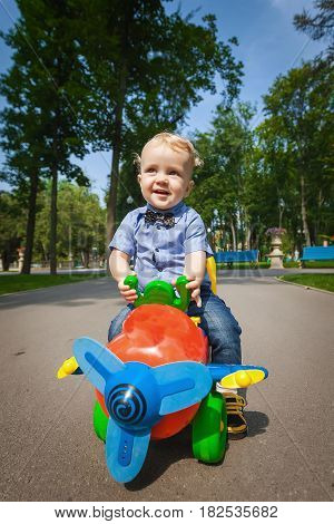 Little blond kid boy driving color toy plane and having fun outdoors. Child enjoying warm summer day in nature landscape