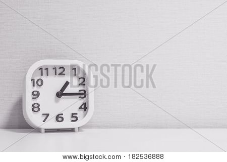 Closeup white clock for decorate show a quarter past one o'clock or 1:15 p.m. on white wood desk and cream wallpaper textured background in black and white tone with copy space