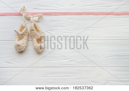 Knitted booties baby girl on a white wooden background. Minimal style. Flat lay. Trendy minimal flat lay concept