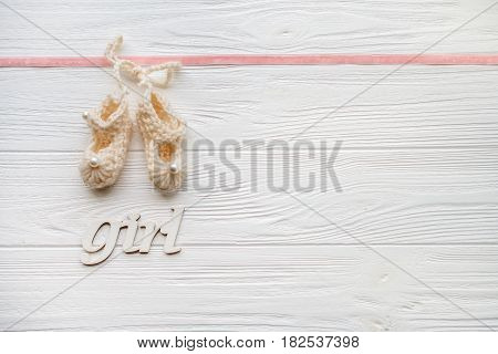 Knitted booties baby and wooden sign girl on a white wooden background. Minimal style. Flat lay. Trendy minimal flat lay concept