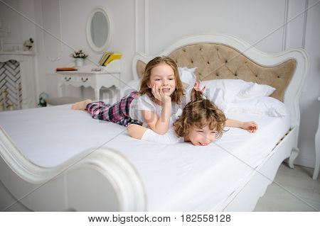 Brother and sister of primary school age play pranks on a bed. Them it is very cheerful.