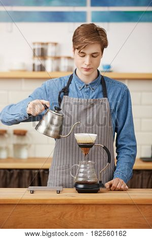 Barista makes pourover coffee pouring water over grounds to extract coffee flavors. Looking focused.