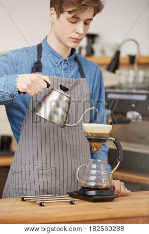 Vertical shot of male barista pouring water through grounds making pourover coffee at bar counter.