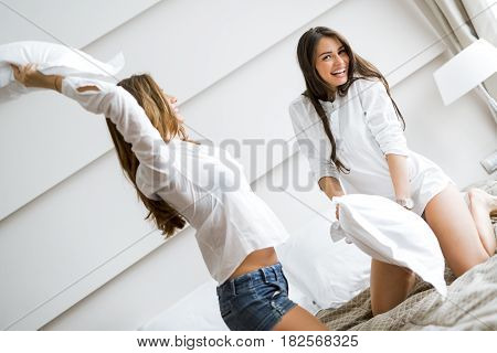 Two beautiful girls fighting with pillows in a luxorious bedroom